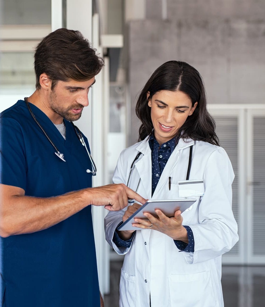 Two healthcare professionals discuss information displayed on a digital tablet in a medical facility.