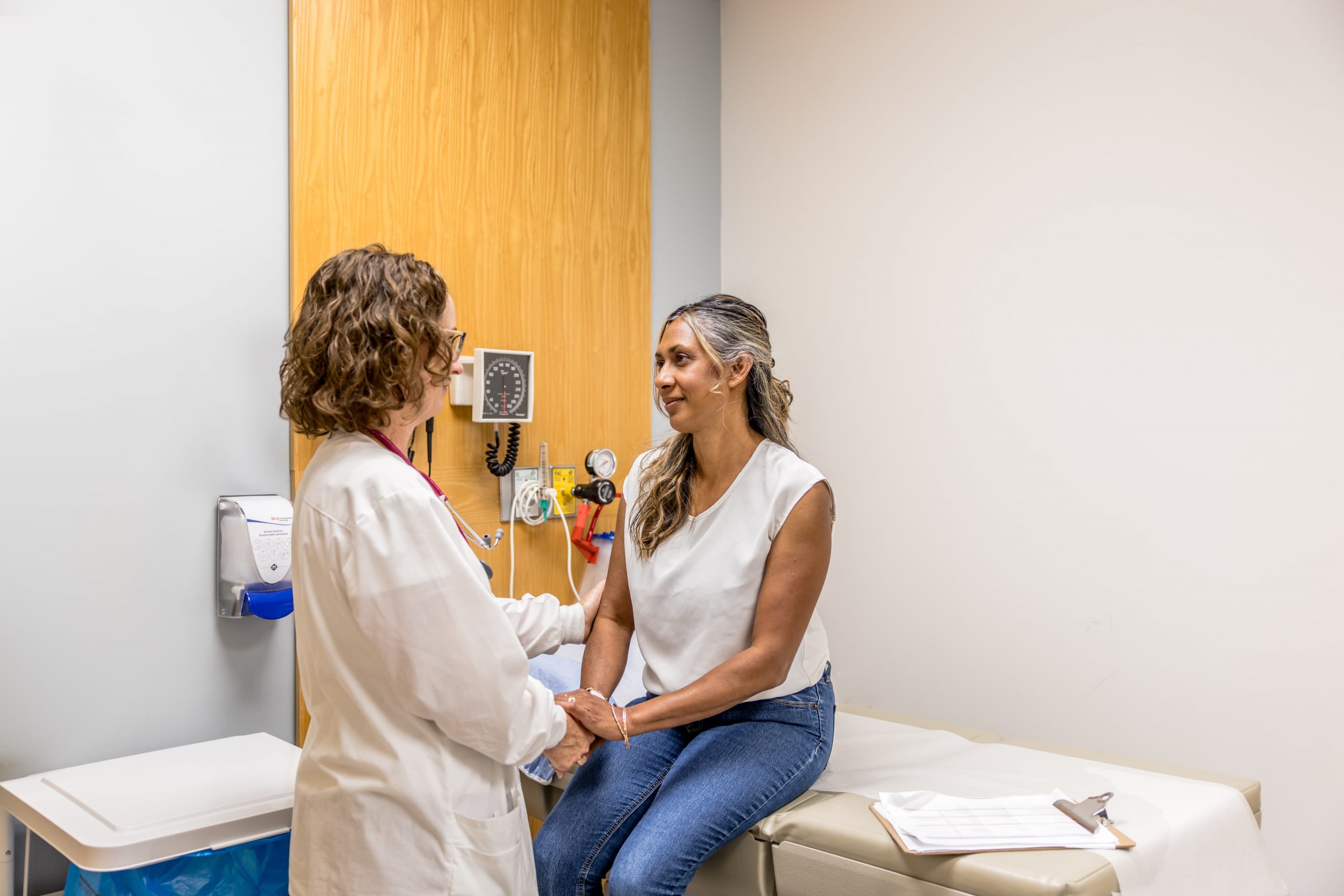 A doctor speaks with a patient seated on an exam table in a medical office.