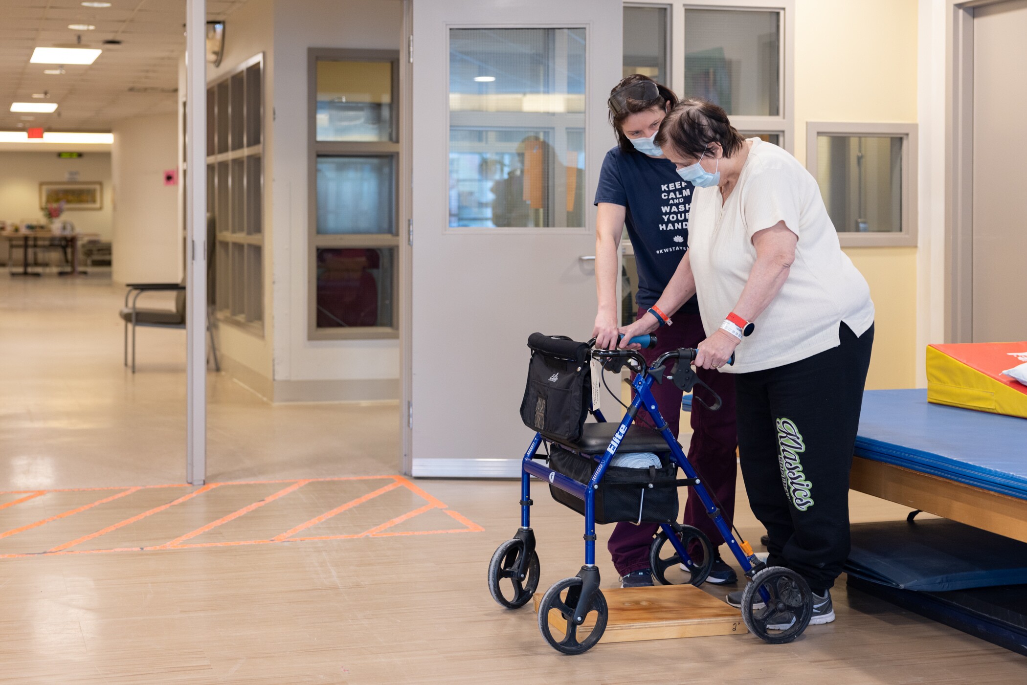 Physical therapist assists a woman using a walker to step up onto a low platform in a clinical setting.