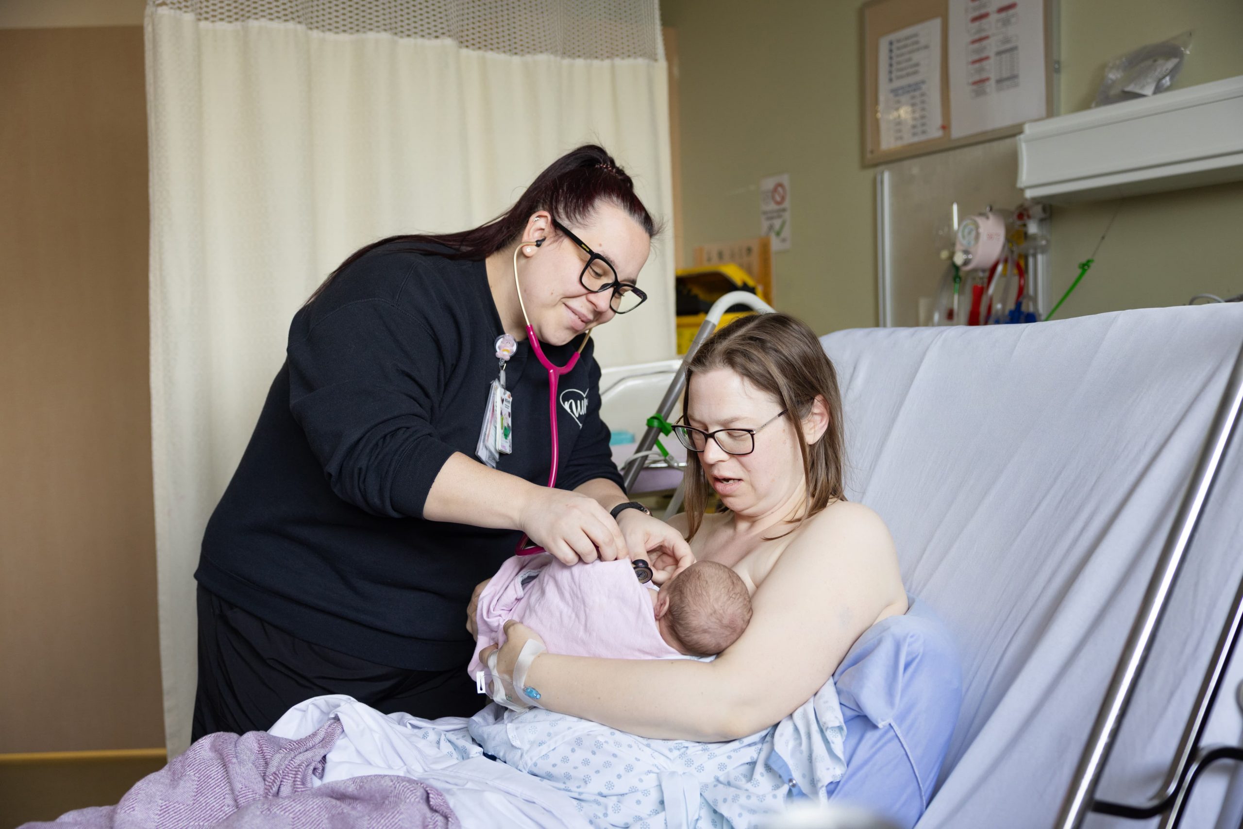 A healthcare professional examines a newborn held by a parent in a hospital bed.