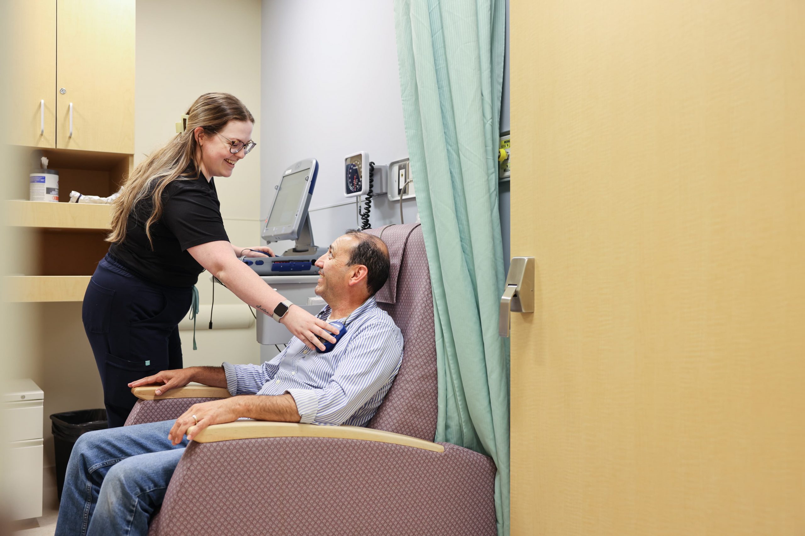 A healthcare worker speaks with a seated patient in a medical examination room.