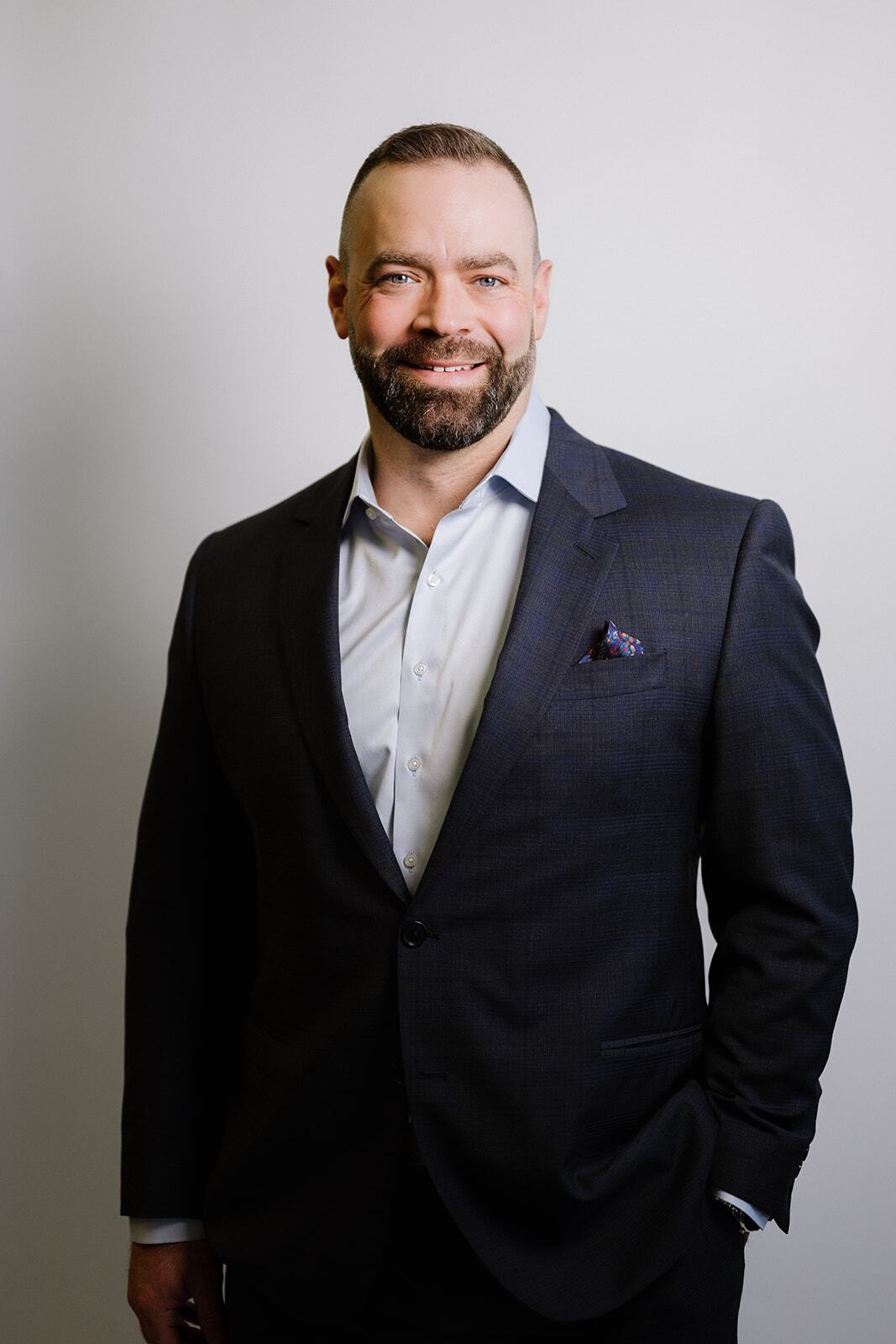 Garth wearing a dark suit and light dress shirt, standing and smiling against a plain light background.