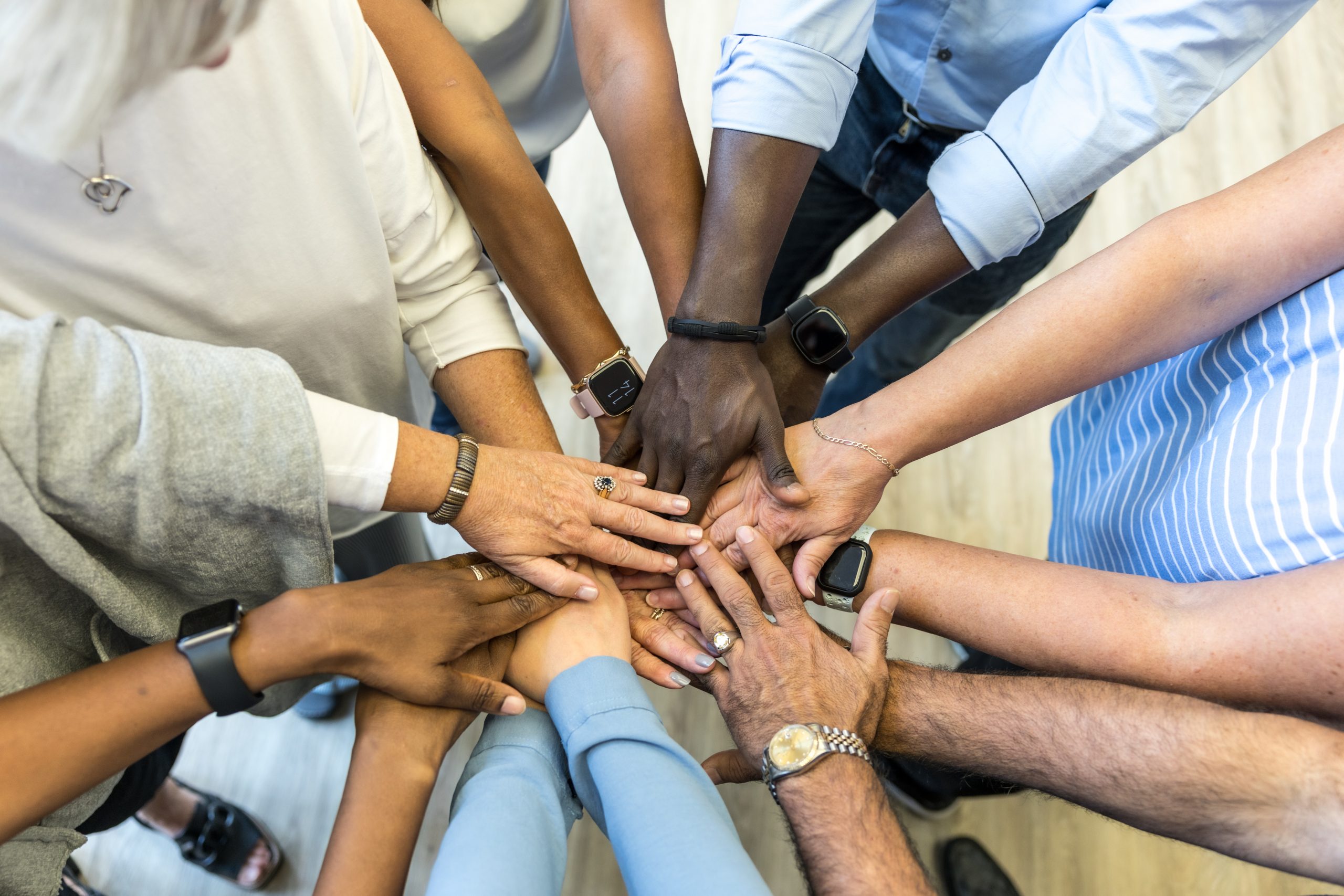 A group of people stand in a circle, stacking their hands together in the center, demonstrating teamwork and unity.