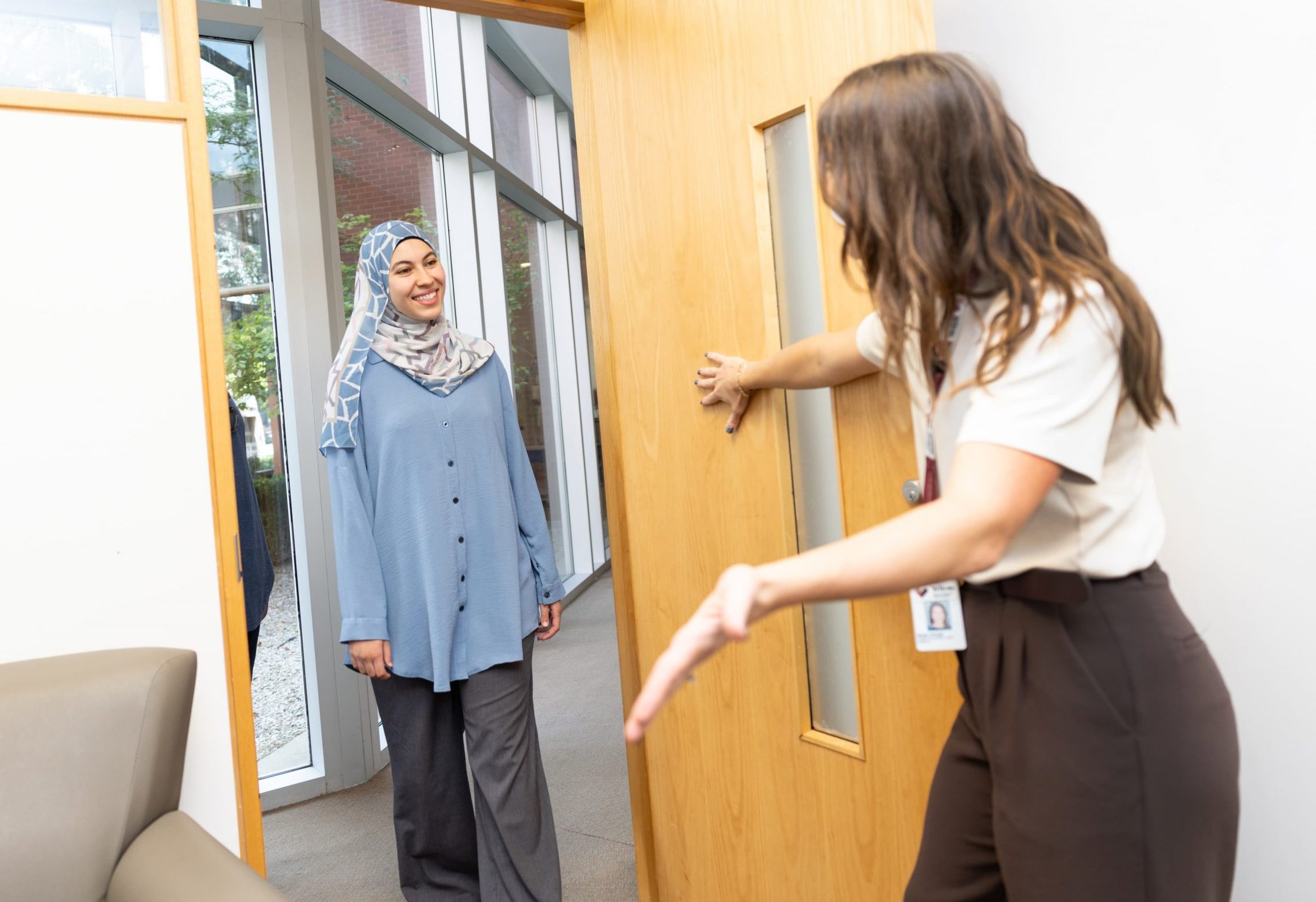 A team members opens a door and gestures to welcome a person wearing a hijab into a bright office space.