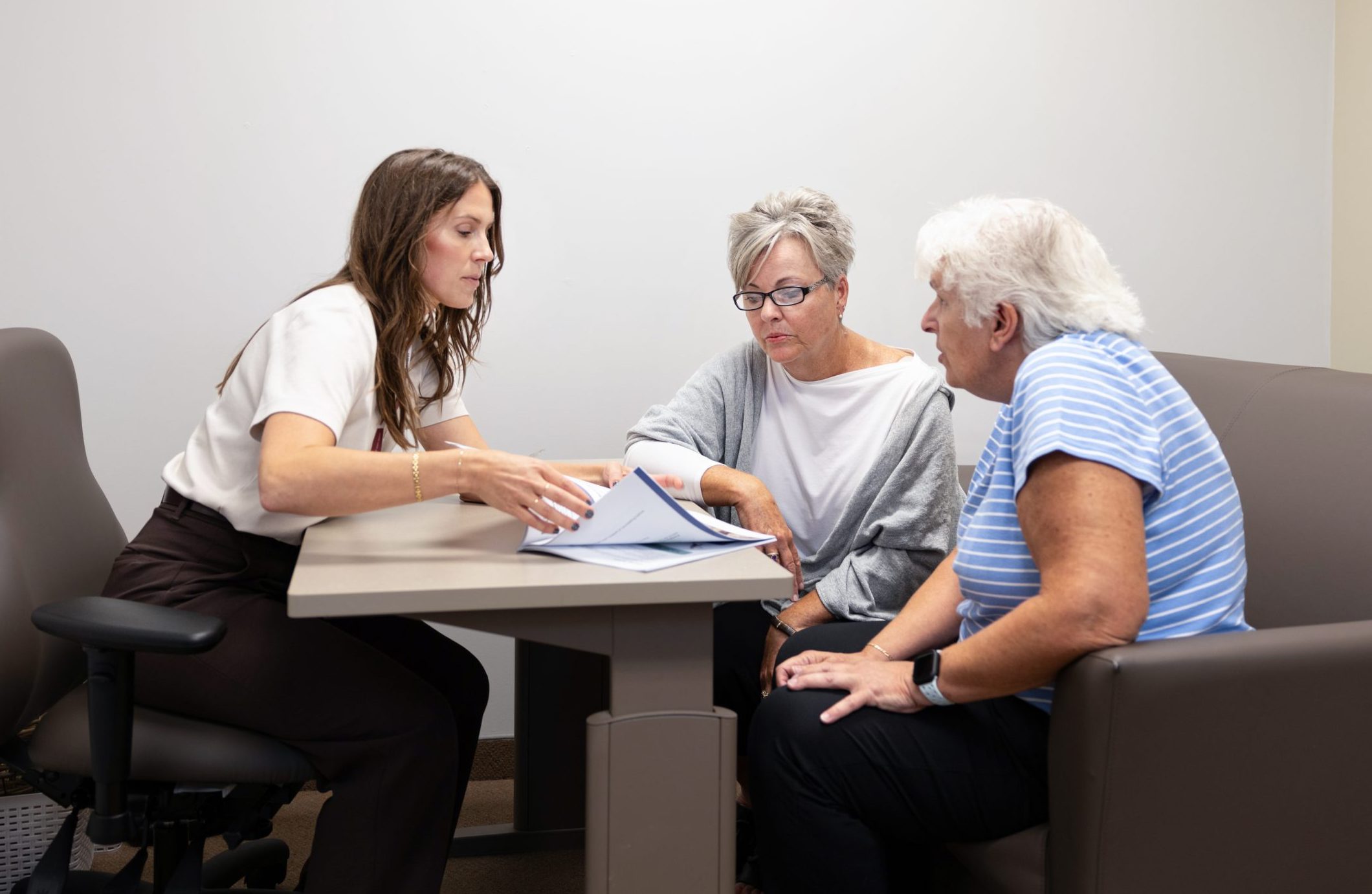 A woman shows documents to two older adults seated at a table in an office setting.