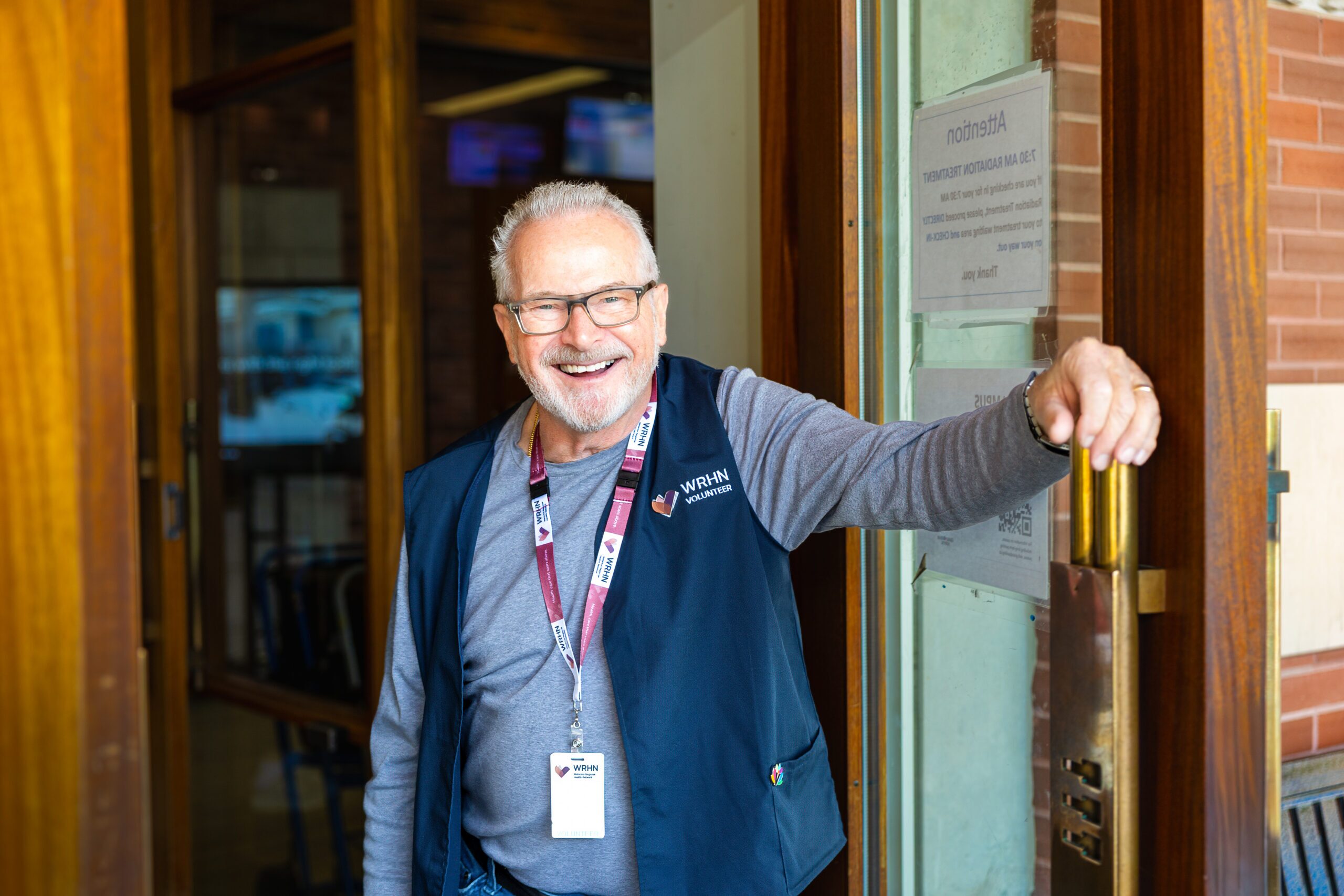 A volunteer holds the door to the Centre Centre open with a big smile on their face.