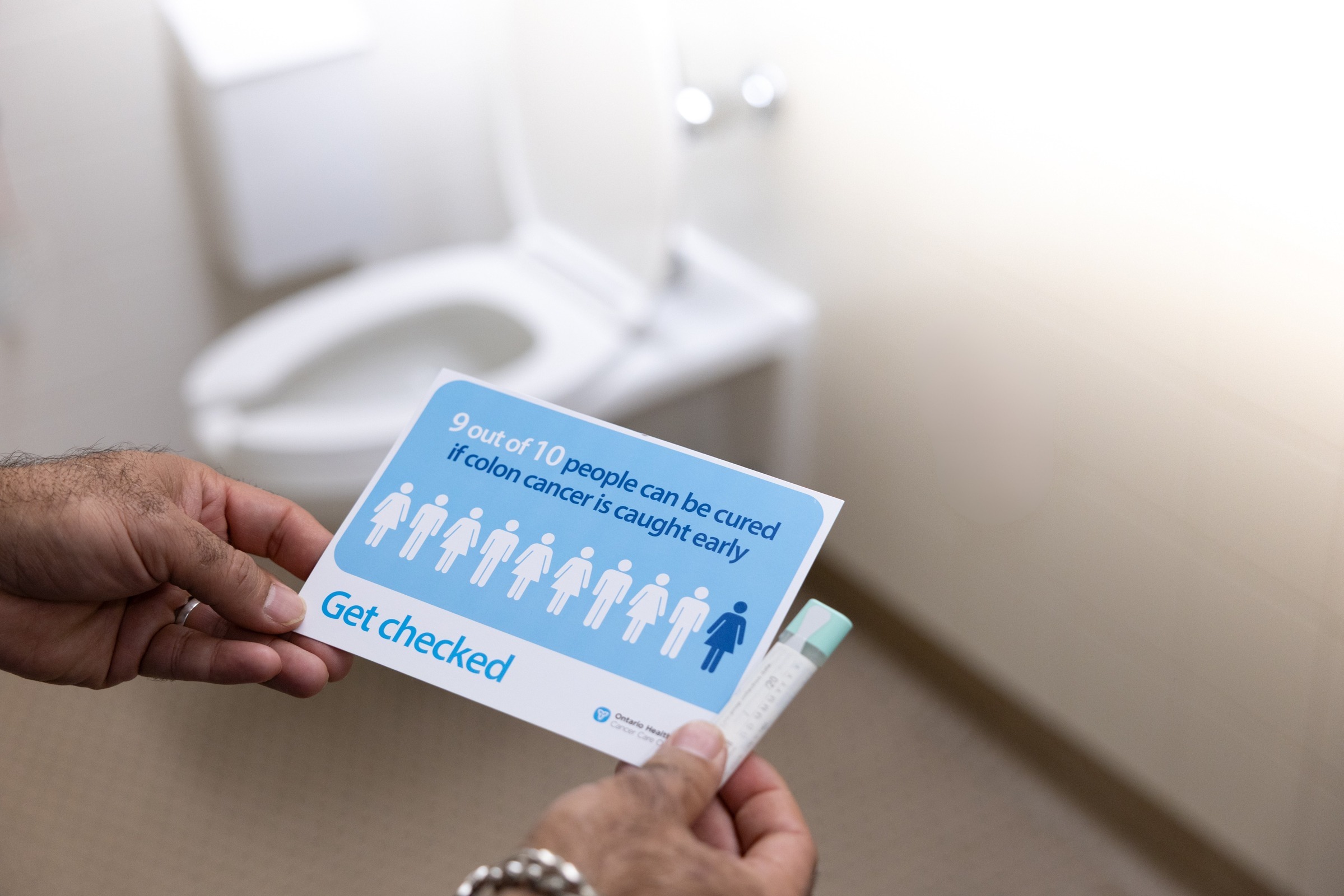 Person holding a FIT test kit and colorectal screening postcard.