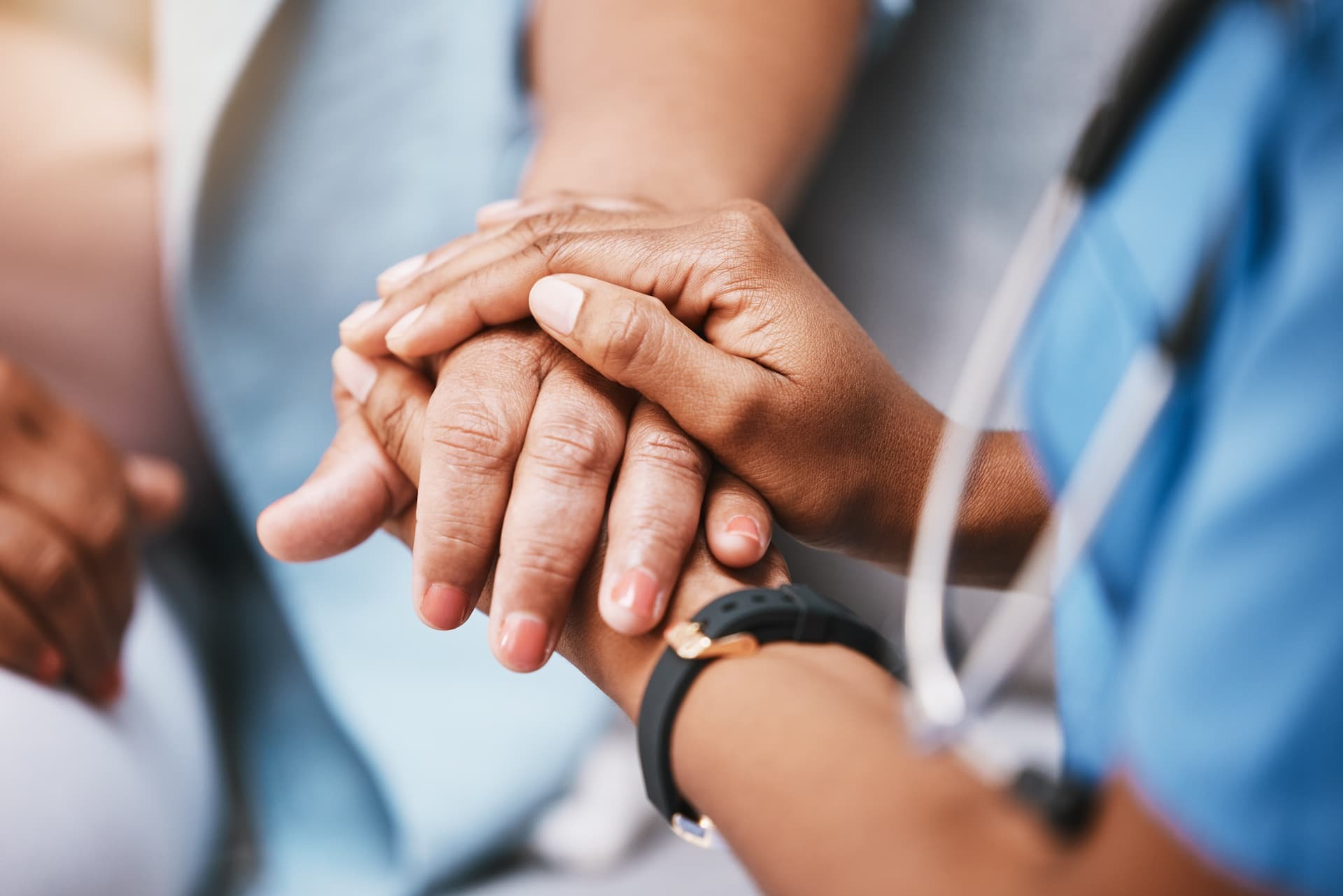 A healthcare worker in scrubs gently holds the hand of a patient in a comforting gesture.
