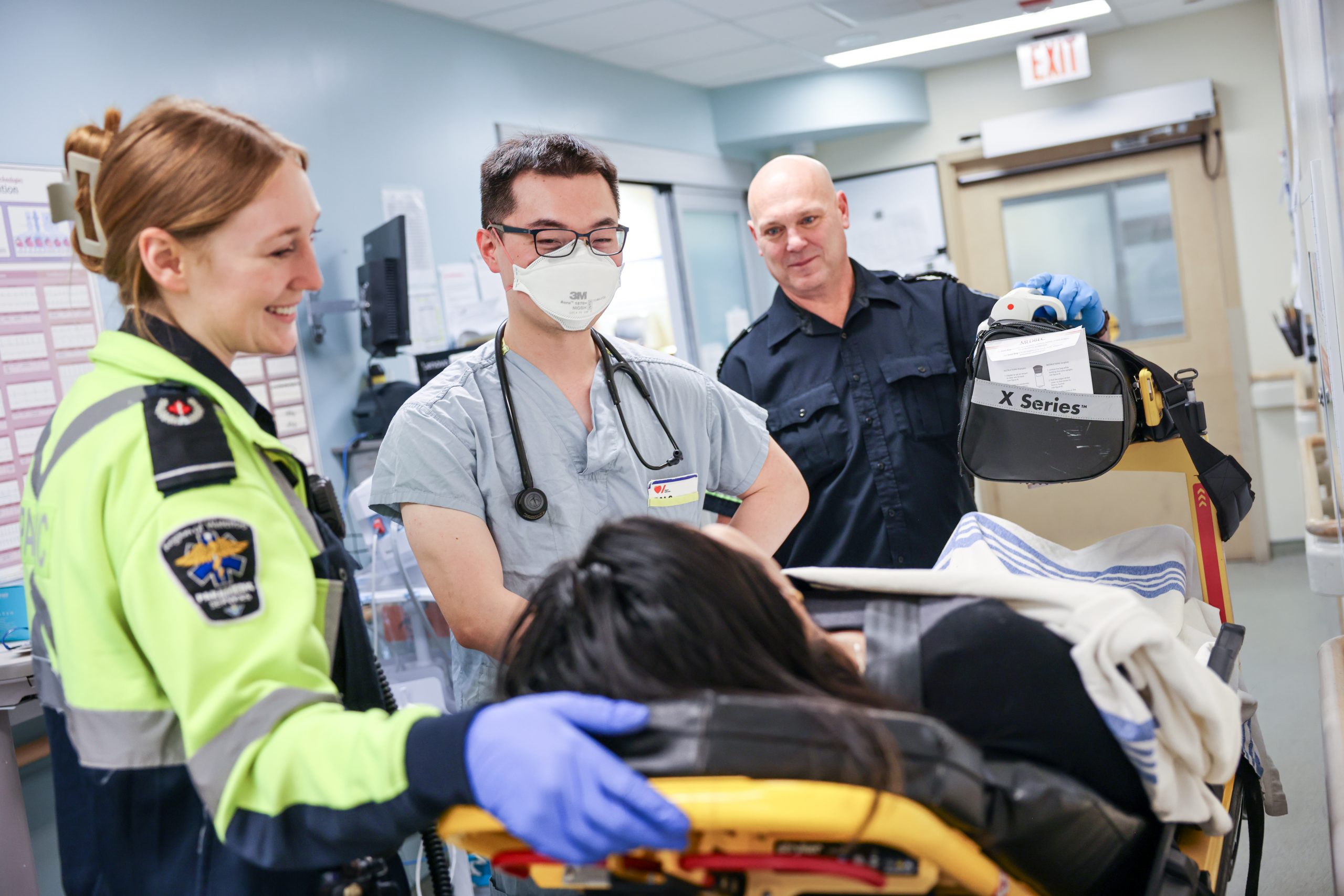 Paramedic and medical staff attend to a patient on a stretcher in a hospital hallway.