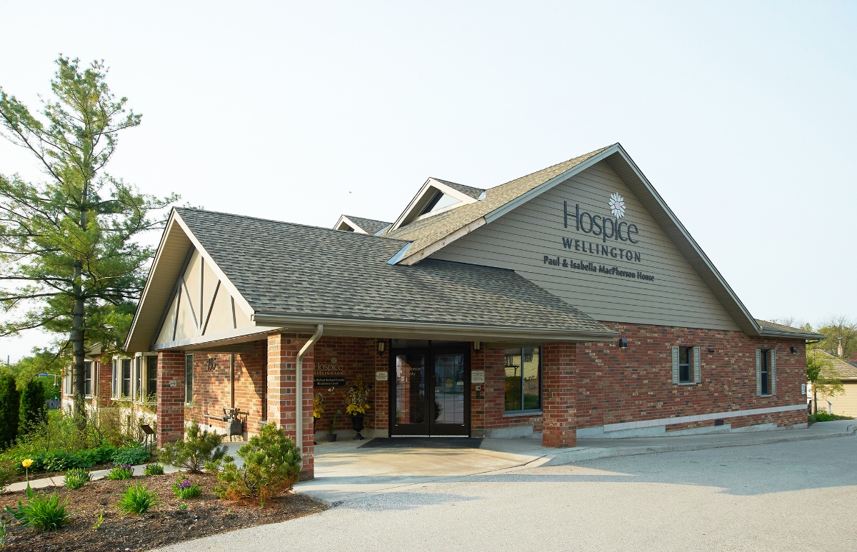 A brick building with the sign "Hospice Wellington" above the entrance on a clear day.