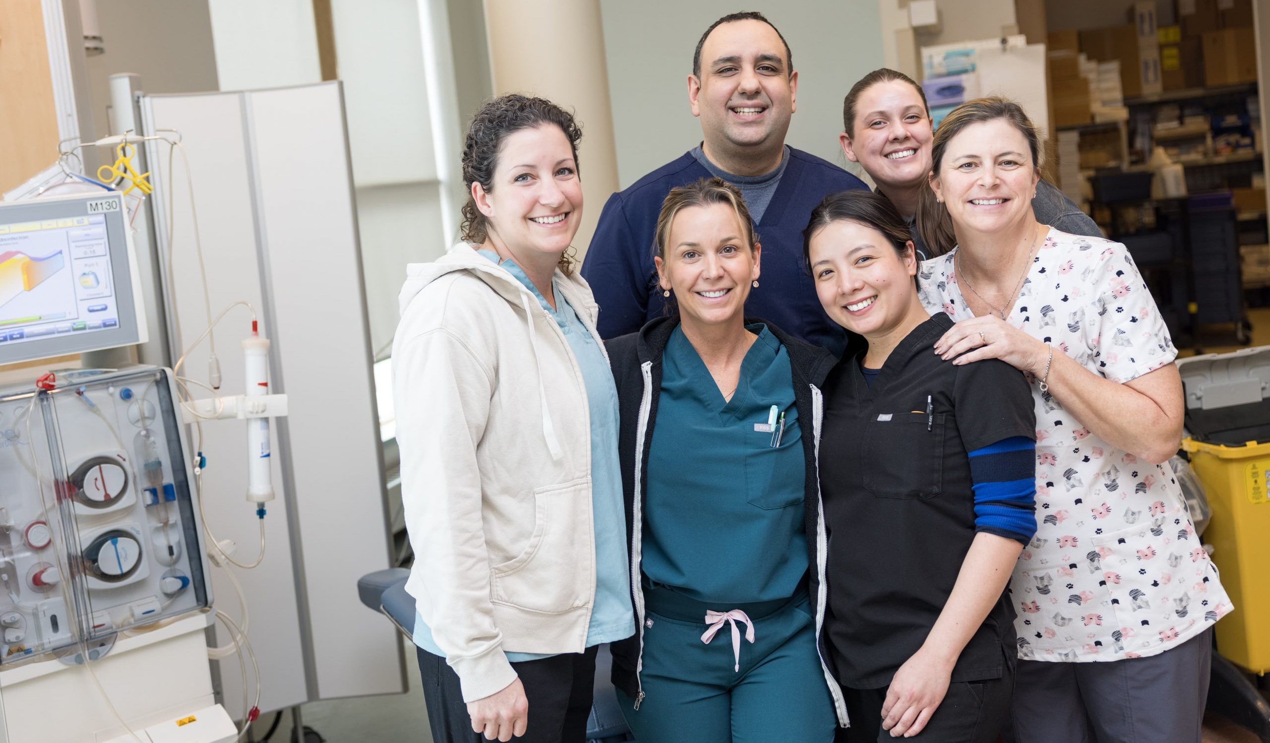 Six healthcare workers stand together and smile for a group photo in a medical facility.