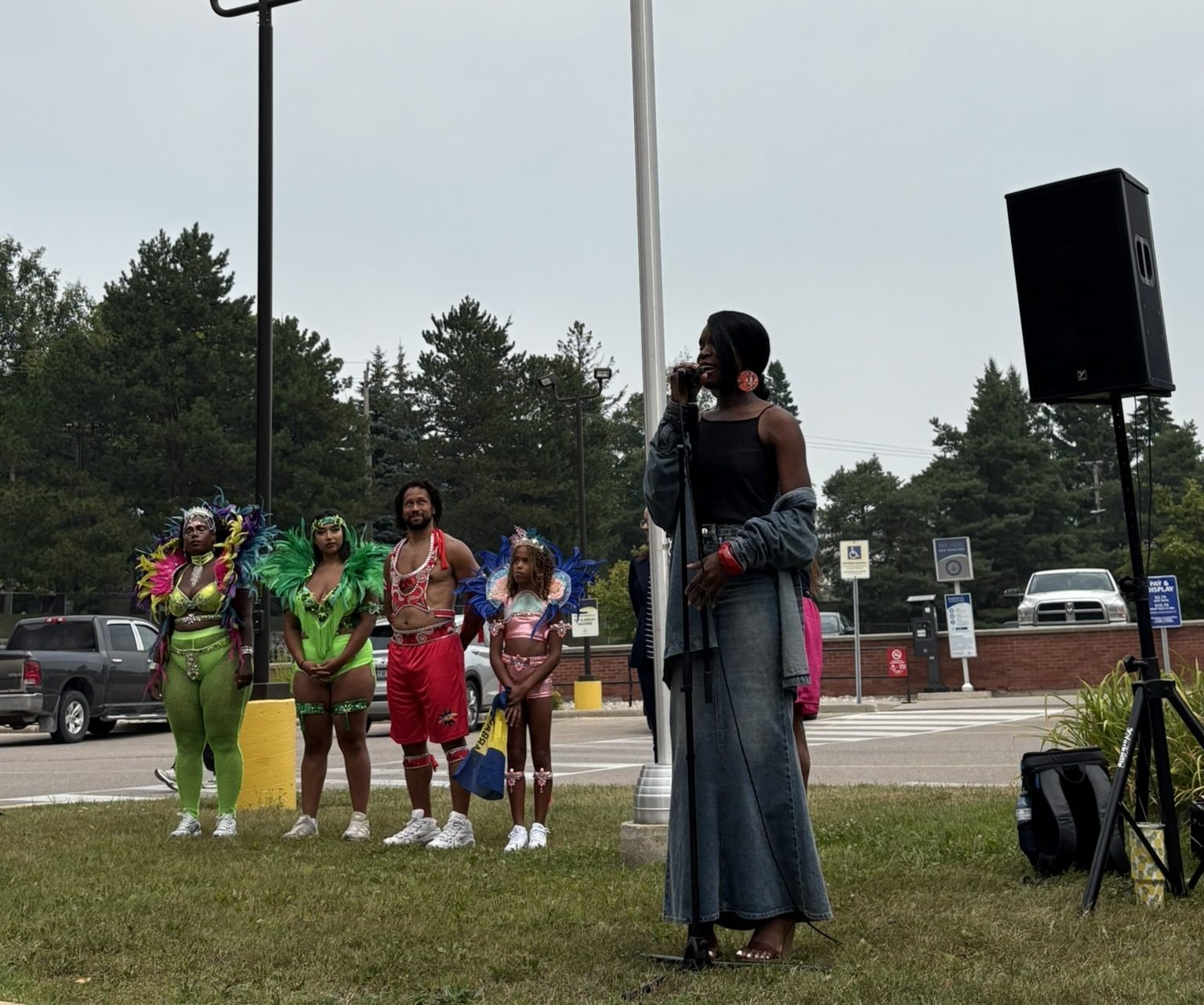 A person speaks at a microphone near a raised Pan-African flag as five people in colorful outfits stand nearby.