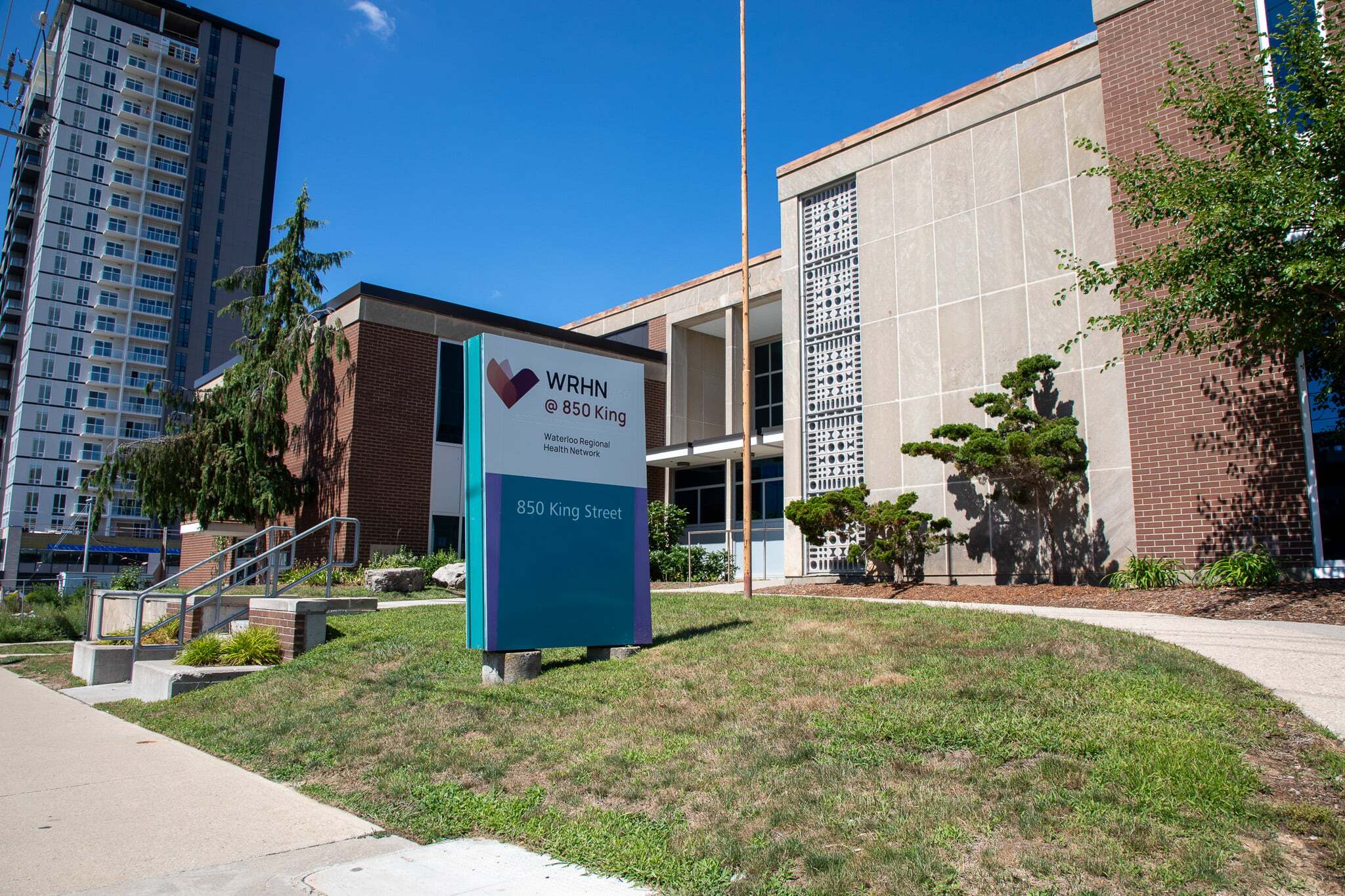 A sign for WRHN @ 850 King stands in front of a modern brick building with a sidewalk and landscaping.