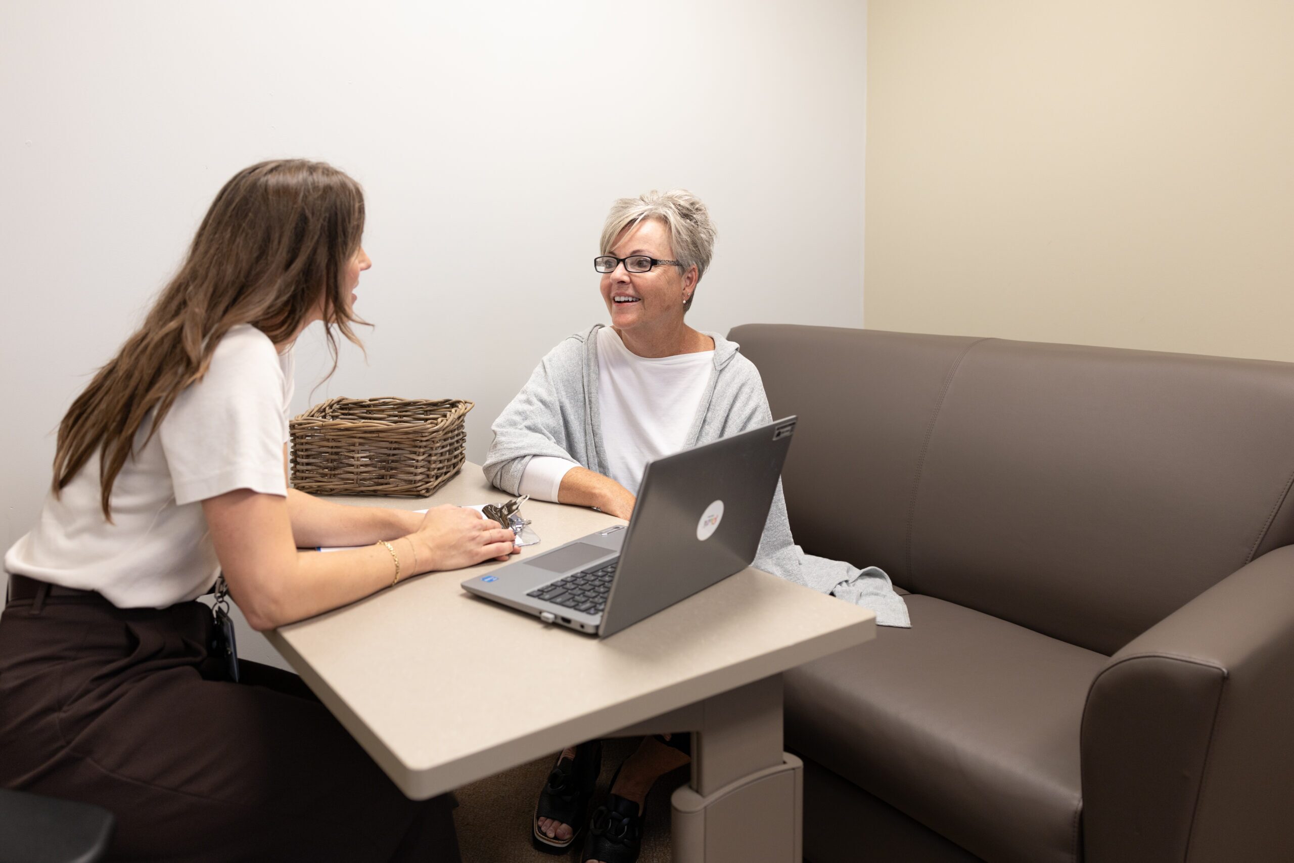 two people sitting at a desk overlooking a laptop with information.