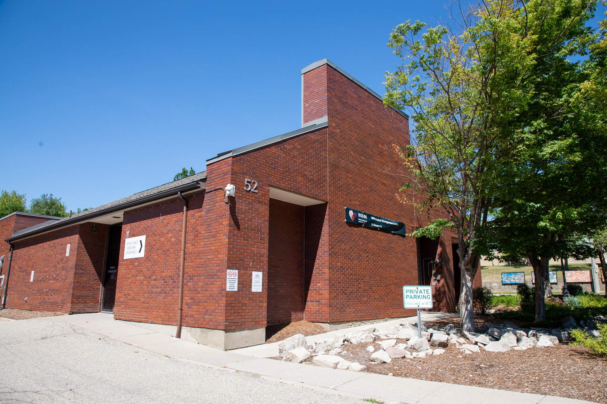 A brick building with the number 52 and signs for private parking and directory information on a sunny day.