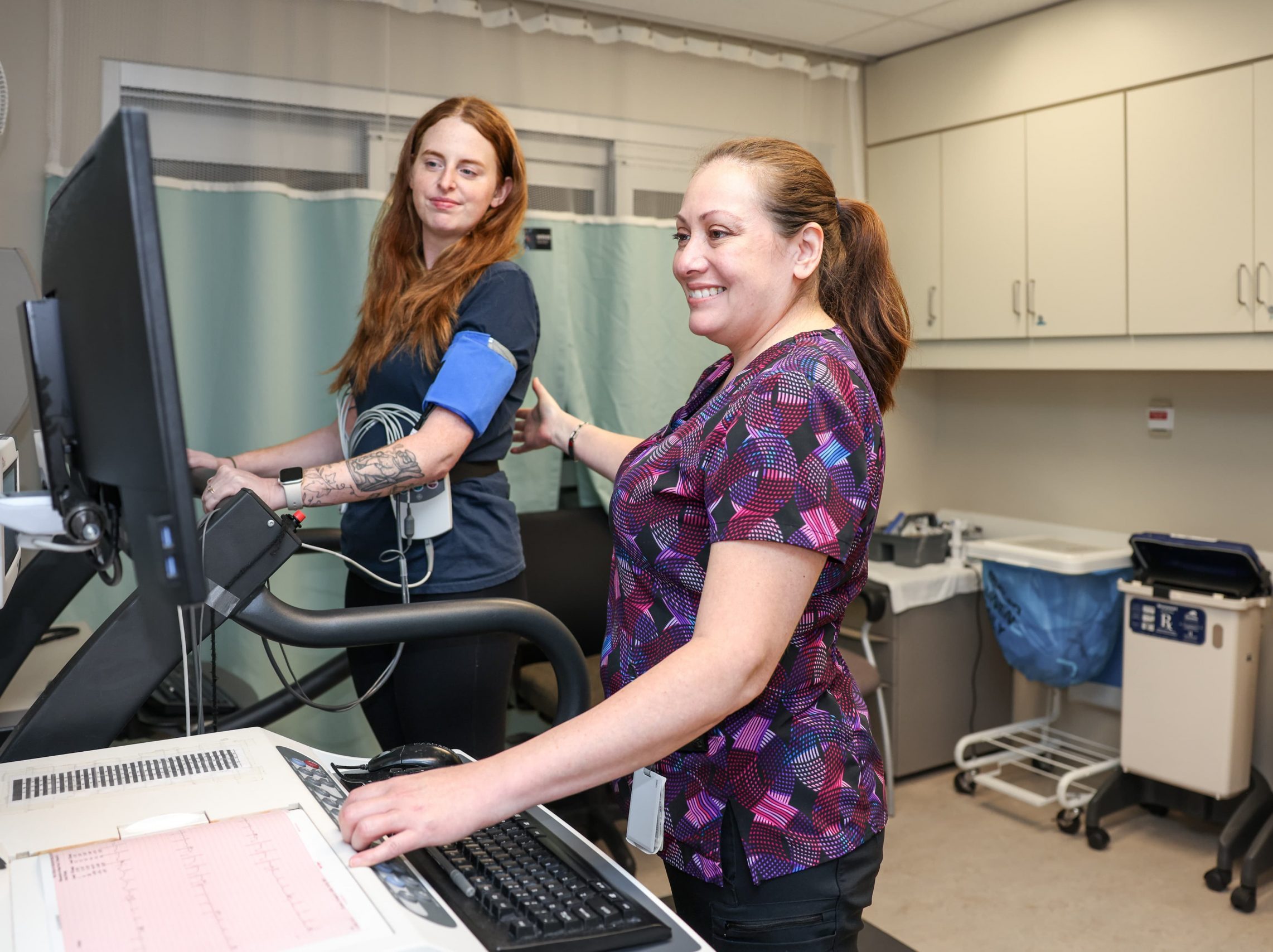 Ein Mitarbeiter des Gesundheitswesens überwacht einen Patienten auf einem Laufband während einer medizinischen Untersuchung in einer klinischen Umgebung.