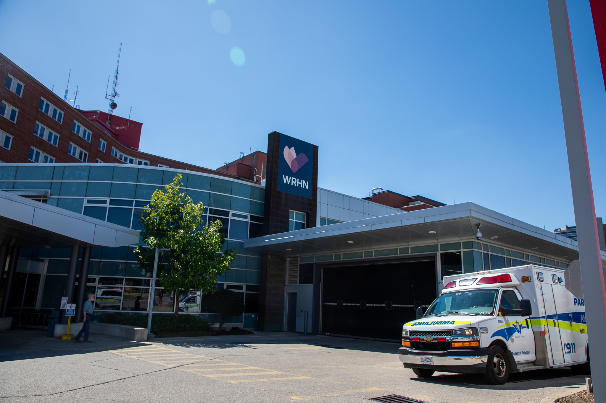 Una ambulancia está estacionada frente a la entrada de un hospital con un letrero de WHRN en un día soleado.