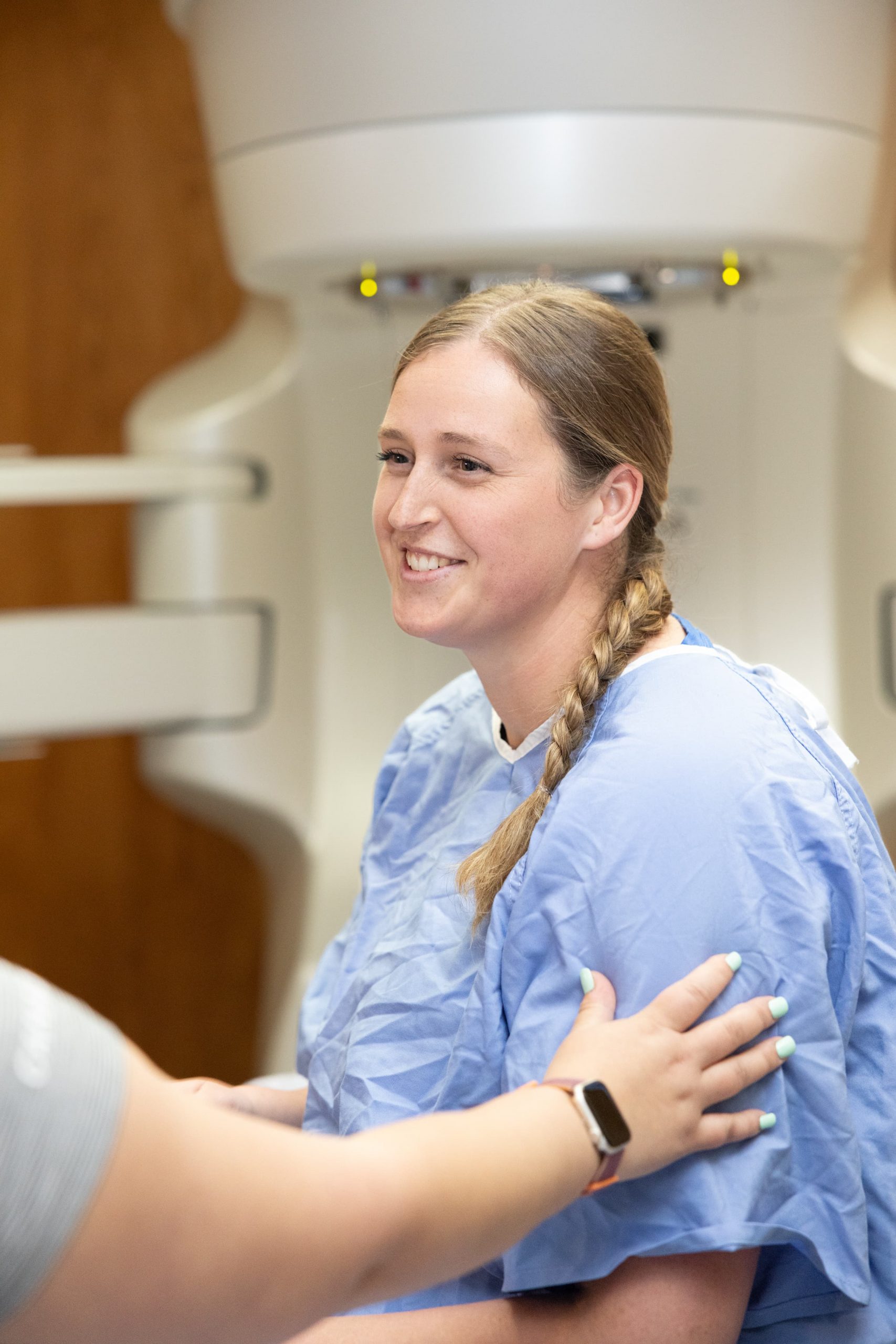 Un patient vêtu d'une blouse d'hôpital est assis et sourit tandis qu'une autre personne lui touche le bras dans un cadre médical.